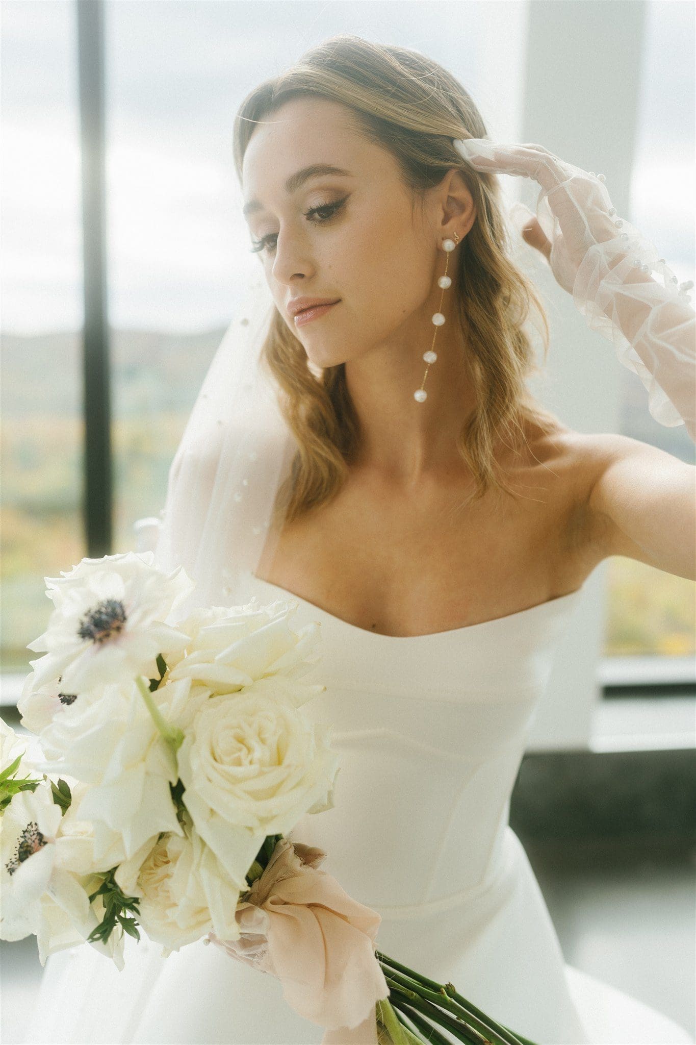 Bride in an elegant white gown holding a classic white rose bouquet with delicate pearls