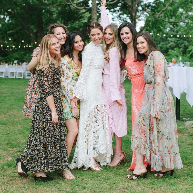 Bride in a lace gown posing with her bridesmaids in colorful dresses at an outdoor wedding